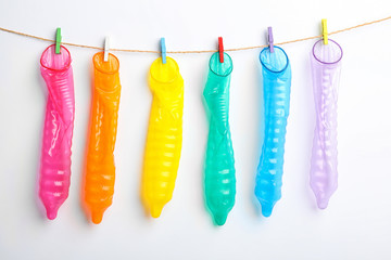 Used colorful condoms hanging on clothesline against white background. Safe sex concept - obrazy, fototapety, plakaty