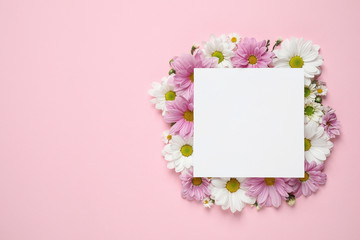 Beautiful chamomile flowers and paper card on pink background, flat lay with space for text