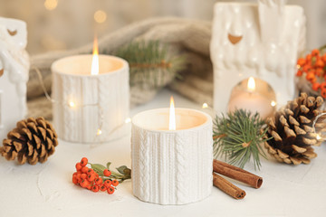 Holders with burning candles and decoration on white table against blurred Christmas lights
