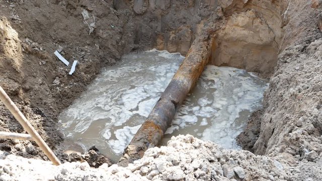 large ditch, trench, pit, hole in the ground with water pipe leakage. utility tube repair fix concept. 4k UHD video footage.