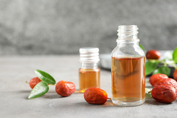 Glass bottle with jojoba oil and seeds on grey stone table. Space for text