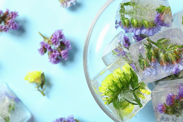 Bowl of ice cubes with flowers on blue background, top view. Space for text