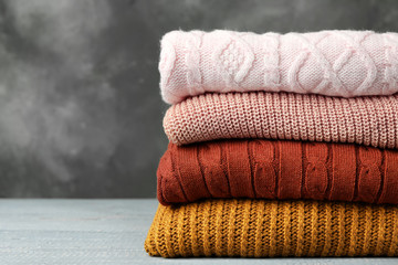 Stack of warm clothes on wooden table against grey background. Autumn season