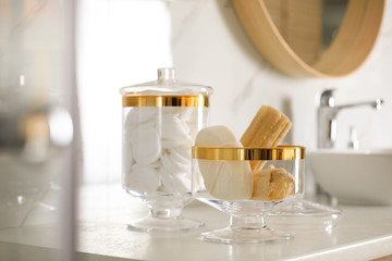 Jars with cotton pads and loofah sponges on countertop in bathroom