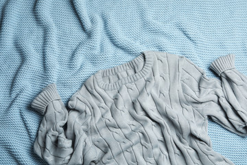Warm grey knitted sweater on light blue blanket, flat lay