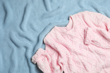 Warm pink knitted sweater on light blue blanket, flat lay