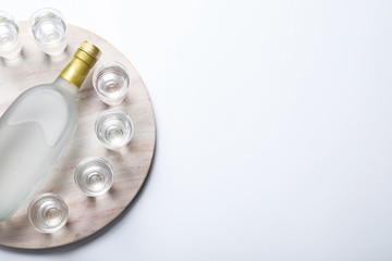Bottle of vodka and shot glasses on white background, top view. Space for text