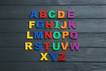 Colorful magnetic letters on black wooden background, flat lay. Alphabetical order