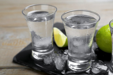 Shots of vodka, lime and ice on wooden table