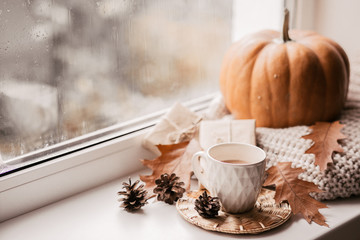 Cup of coffee, pumpkin, dried autumn leaves on window. Autumn composition.