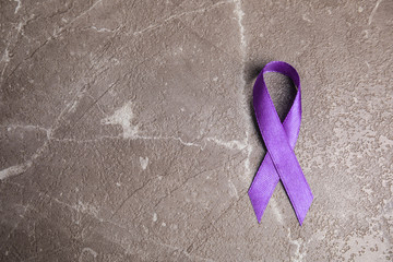 Purple ribbon on stone background, top view with space for text. Domestic violence awareness