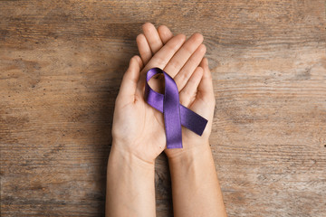Woman holding purple ribbon on wooden background, top view. Domestic violence awareness