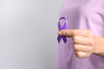 Woman holding purple ribbon on grey background, closeup with space for text. Domestic violence...
