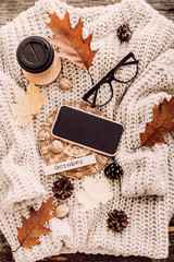 Cup of coffee, nuts, glasses, dried autumn leaves on sweater background. Autumn composition.