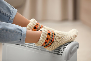 Woman warming feet on electric heater at home, closeup