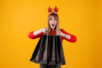 excited woman with gifts in holiday shopping bags wearing funny hoop isolated over yellow