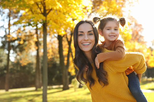 Happy woman with little daughter in sunny park. Autumn walk