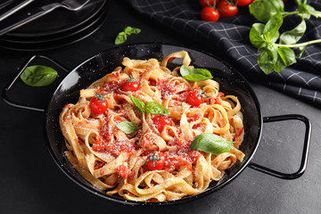 Tasty pasta with tomatoes, cheese and basil on black table