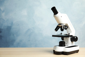 Modern microscope on wooden table against blue background, space for text. Medical equipment