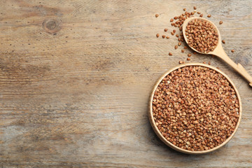 Bowl and spoon of uncooked buckwheat on wooden table, flat lay. Space for text