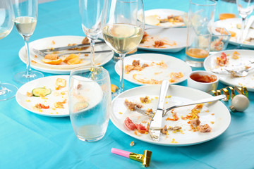 Dirty tableware with leftovers on light blue cloth after party