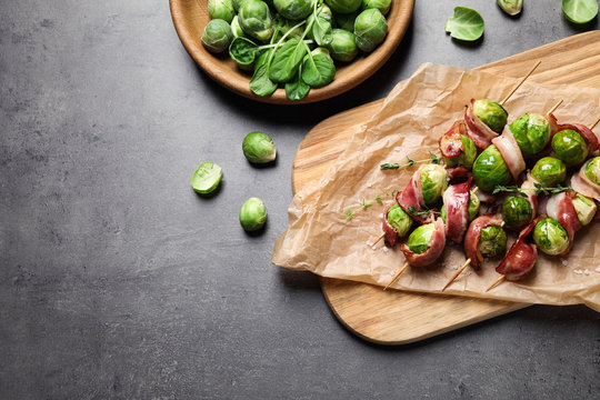 Skewers with Brussels sprouts and bacon served on grey table, flat lay. Space for text