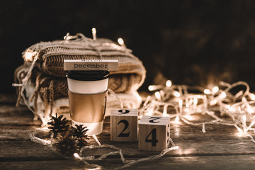 Winter composition. Cup with coffee, garland, book, cones on a wooden background.