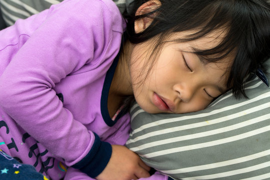 Little Asian child girl sleeping on couch with purple color pajamas