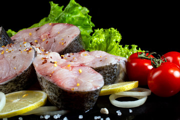 fish steaks with lettuce spices and tomatoes on a black background