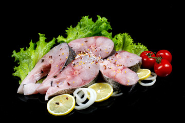 fish steaks with lettuce spices and tomatoes on a black background