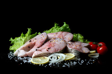 fish steaks with lettuce spices and tomatoes on a black background