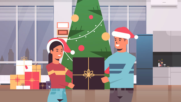 couple holding gift present box merry christmas happy new year holiday celebration concept man woman wearing santa hats standing near fit tree modern living room interior horizontal portrait vector