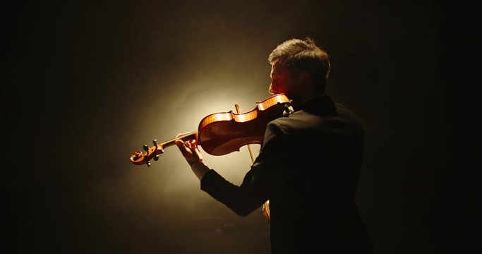 Male violin player having a solo on stage. Professional musician wearing tux is spotted by light on black background 4k footage