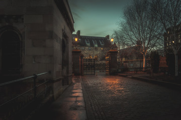 Fototapeta na wymiar GLASGOW, SCOTLAND, DECEMBER 16, 2018: Creepy cobbled street surrounded by old European style buildings. Illuminated only with weak light from street lamps.