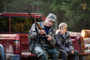 Father and son sitting in a pickup truck after hunting in forest. Dad showing boy mechanism of a shotgun rifle. - 300250837