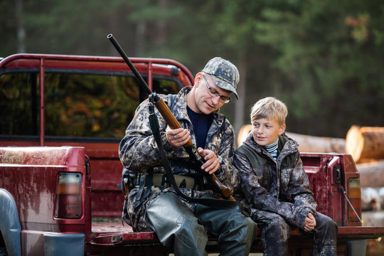 Father and son sitting in a pickup truck after hunting in forest. Dad showing boy mechanism of a shotgun rifle.