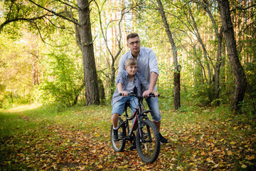 Obraz premium Excited father and his son having fun together at the green park, teaching son how to ride a bicycle