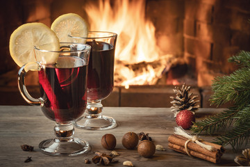 Two glasses of mulled wine on a wooden table near a Christmas tree in front of a burning fireplace