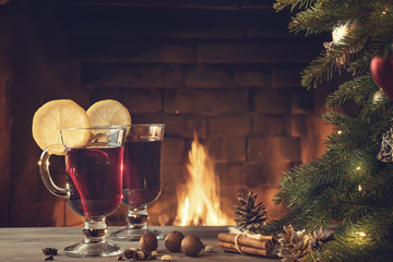 Two glasses of mulled wine on a wooden table near a Christmas tree in front of a burning fireplace