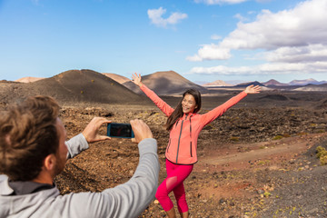 Tourists taking picture vlogging outside on Europe travel, girl posing for boyfriend with arms up having fun on Timanfaya National Park, Lanzarote, Canary Islands.