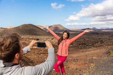 Wall murals Canary Islands Tourists taking picture vlogging outside on Europe travel, girl posing for boyfriend with arms up having fun on Timanfaya National Park, Lanzarote, Canary Islands.