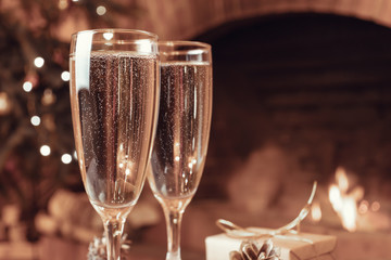 Two glasses with champagne on a wooden table in a room with a burning fireplace