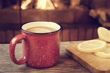 Red mug with hot tea with lemon in front of a burning fireplace, comfort and warmth of the hearth concept