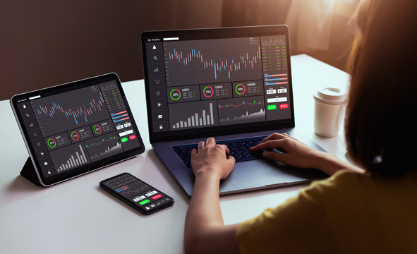 Stock exchange market concept, businesswoman trader looking on laptop and tablet, smartphone with graphs analysis candle line in office room, diagrams on screen.