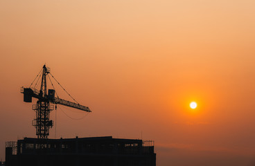 Crane building construction site at sunset or sunrise. High-quality stock photo image silhouette of construction tower crane in sunset sky background. Building construction with crane during sunset
