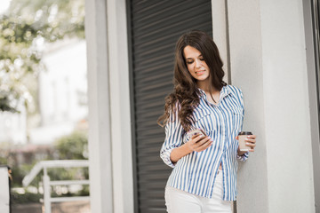 Fototapeta premium Businesswoman uses a phone, walking along the city streets with coffee in her hand.
