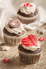 Muffins and chocolate and red heart shaped sweets on a wooden background.