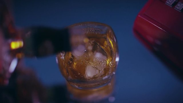 Pouring brown liquor into a shot glass with ice cubes