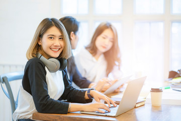 Young Asian girl listening the music with headphones and reading books while sitting at the table in the modern working space.