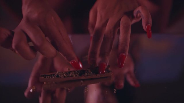 Close-up of a woman’s hands rolling marijuana in cigar paper